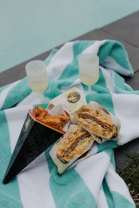 Burgers and fries served by the pool at Château de Jalesnes, a relaxed summer lunch setup on a striped towel.