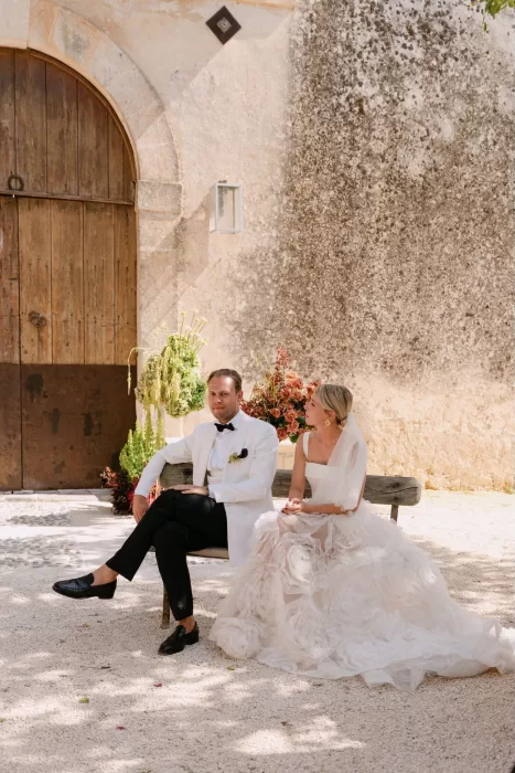 Bride and groom seated on a wooden bench against the textured stone walls of Dimora Delle Balze after the ceremony.