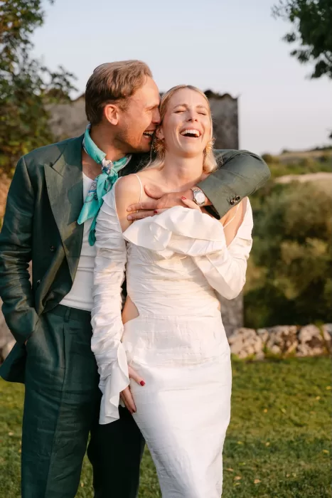 Groom laughing and embracing bride in white gown during golden hour at Dimora Delle Balze.