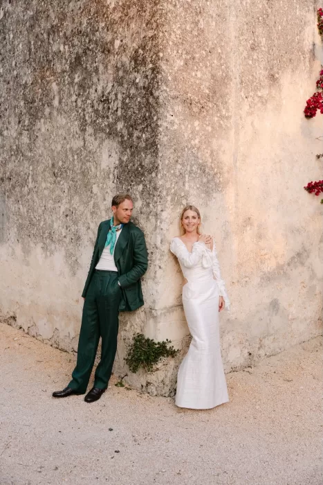 Stylish wedding couple posing against rustic stone walls and bougainvillea at Dimora Delle Balze.