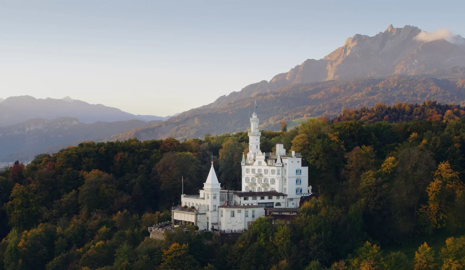 Hotel Château Gütsch perched on a hillside with autumn foliage and mountain views in Lucerne.