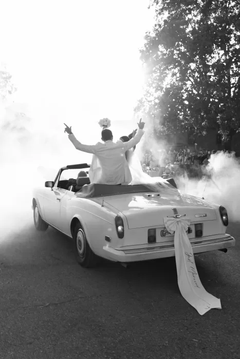 Bride and groom celebrating in their classic convertible as they drive away from Mas del Sord in a cloud of smoke.