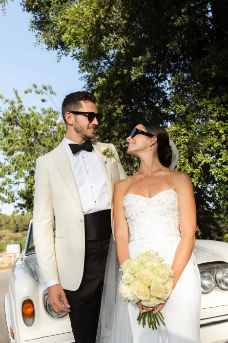 Bride and groom smiling at each other beside their vintage white car at Mas del Sord.
