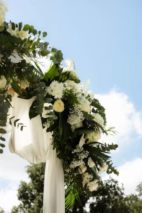 Lush white and green floral ceremony arch at Mas del Sord against a bright summer sky.