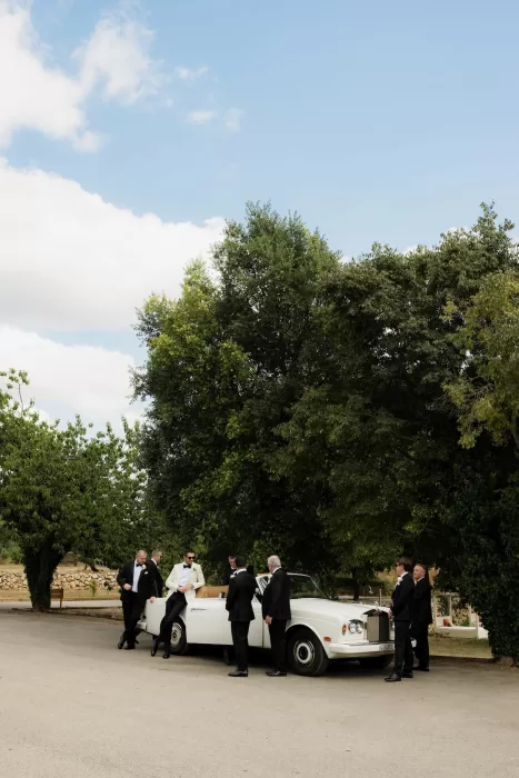 Groom and groomsmen gathered around a vintage white car beneath the trees at Mas del Sord.