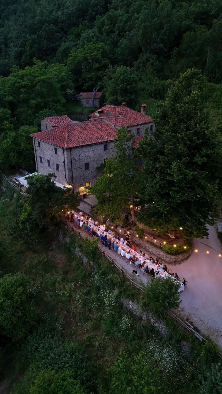 Aerial view of long dinner table lit by string lights outside the stone farmhouse at Novanta 90