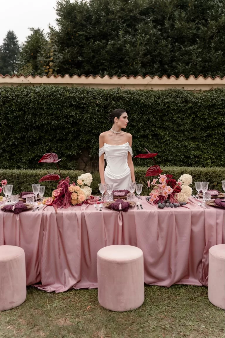 Elegant bride in white gown standing at a pink-toned outdoor wedding table at Villa Buttafava.