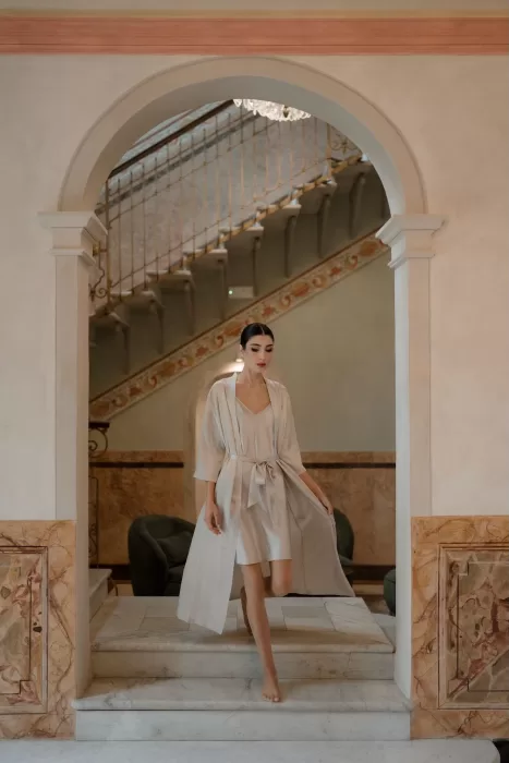 Bride in elegant satin robe walking through the grand hallway with marble stairs at Villa Buttafava.