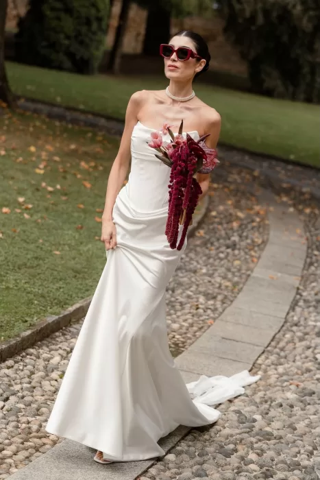 Stylish bride in a satin gown and red sunglasses holding a bold magenta bouquet at Villa Buttafava.