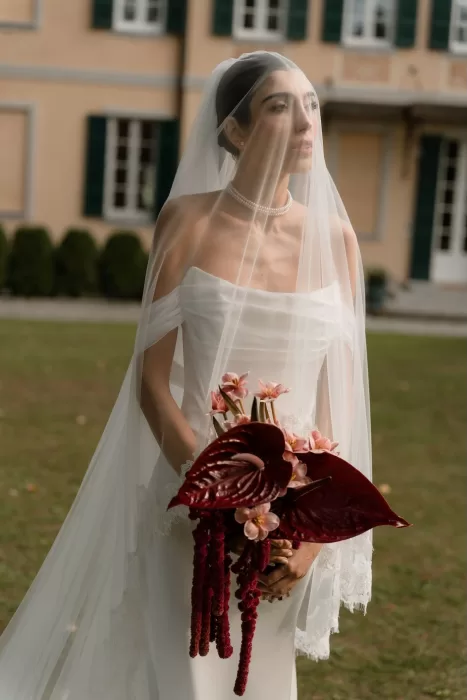 Romantic bridal portrait with pearl necklace and deep red bouquet beneath a veil at Villa Buttafava.