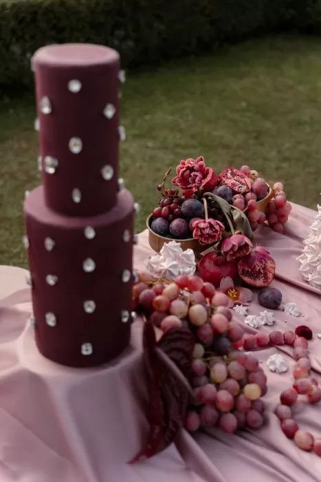 Artistic dessert display with jewel-toned fruits, florals, and meringues on blush satin at Villa Buttafava.