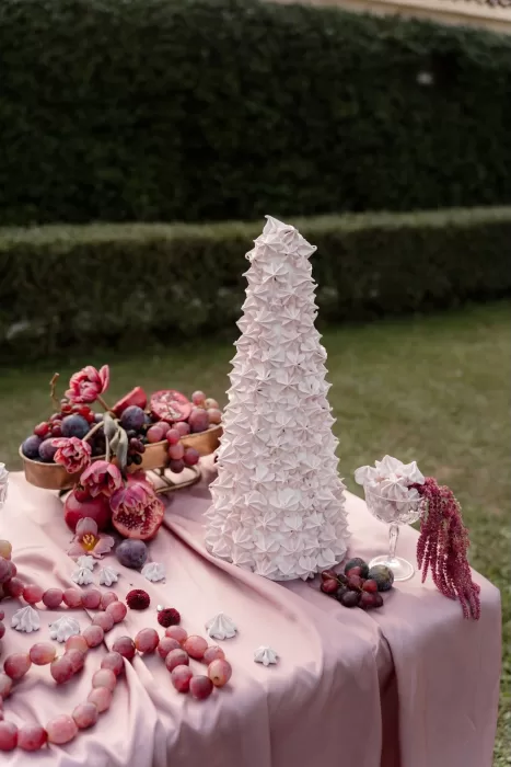 Whimsical dessert display with pink meringue tower and grapes styled on a blush tablecloth at Villa Buttafava.