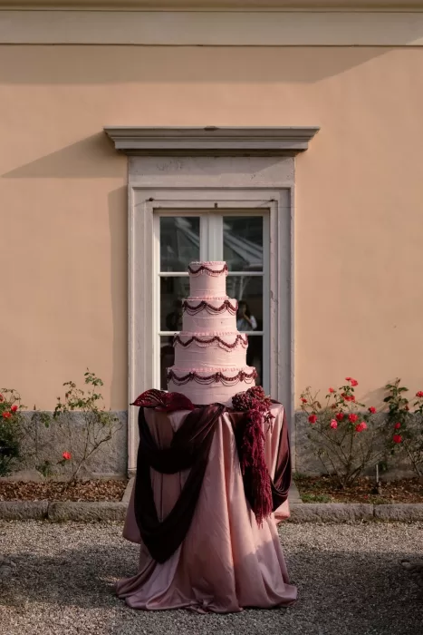 Pink tiered wedding cake with burgundy draping and floral details set against the villa’s peach facade at Villa Buttafava.