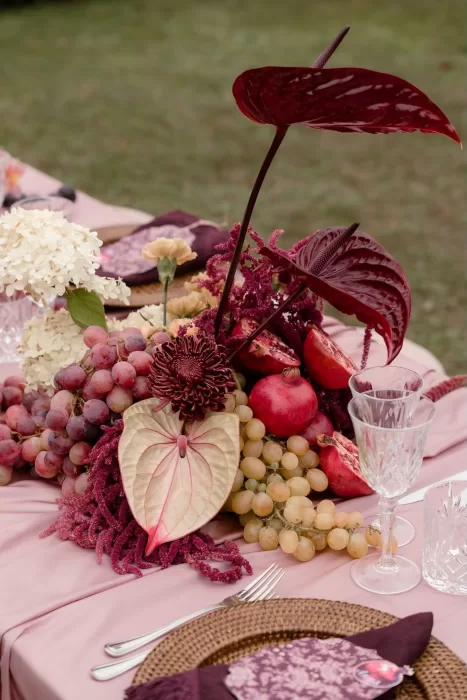 Vibrant wedding table centerpiece with grapes, pomegranates, and anthuriums in deep red tones at Villa Buttafava.