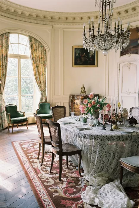 Elegant dining room at Château du Prieuré with lace-draped table, crystal chandelier, and soft morning light filling the space.