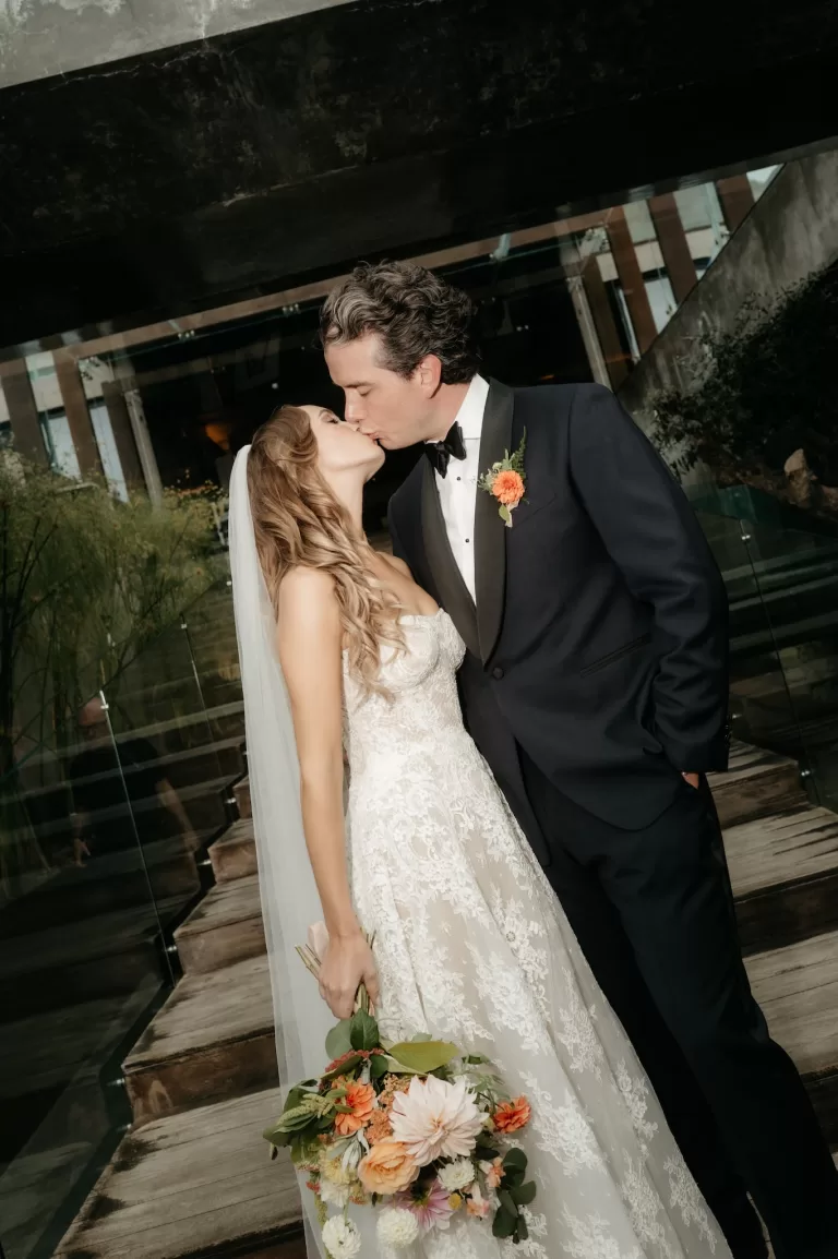Bride and groom kissing beside the modern glass and concrete architecture at Areias do Seixo.