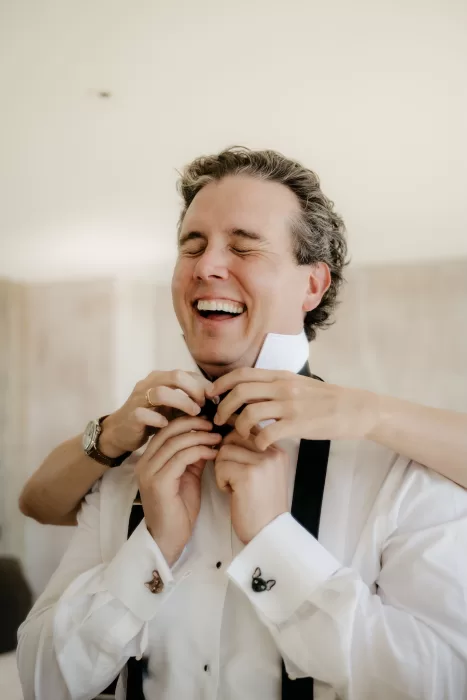 Groom laughing while getting ready with help from friends during morning preparations at Areias do Seixo.