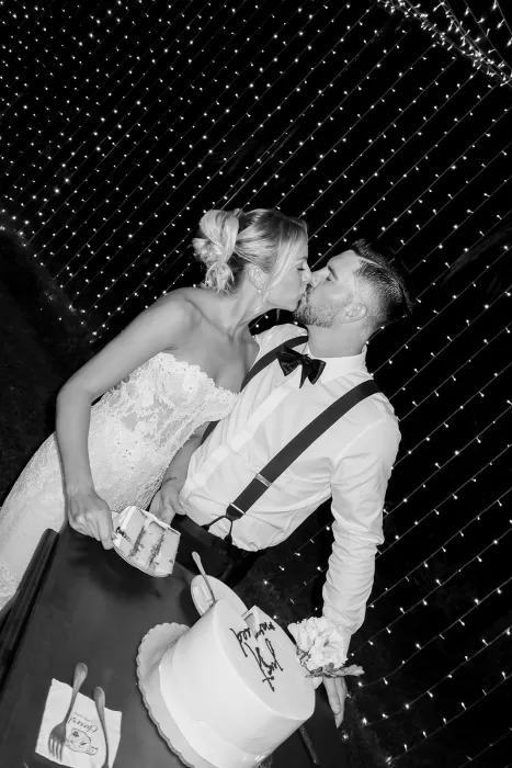 Bride and groom sharing a kiss while cutting their wedding cake at Baja Luna, captured under twinkling lights.