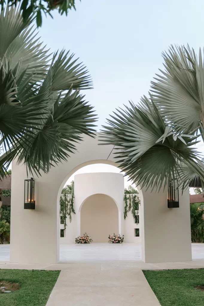 Palm-framed ceremony arch at Baja Luna with sculptural white architecture and floral arrangements.