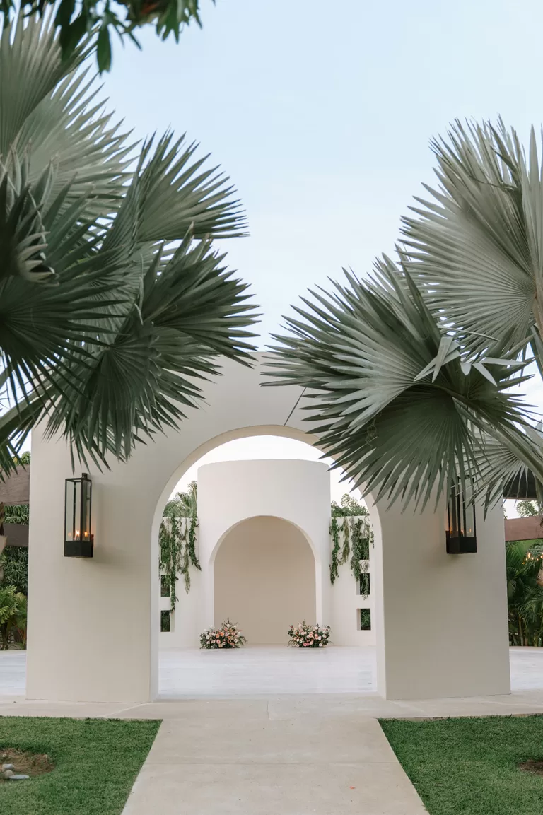 Palm-framed ceremony arch at Baja Luna with sculptural white architecture and floral arrangements.