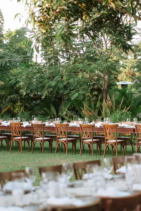 Long outdoor wedding dinner table at Baja Luna surrounded by lush tropical gardens and wooden chairs.