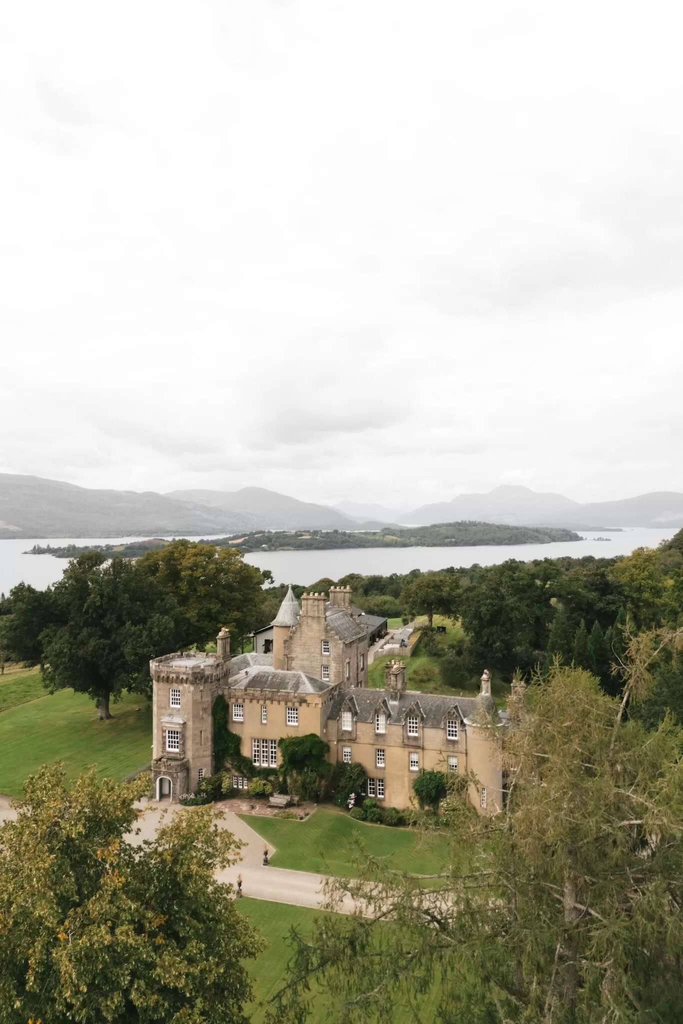 Aerial view of Boturich Castle surrounded by greenery with Loch Lomond stretching into the distance.