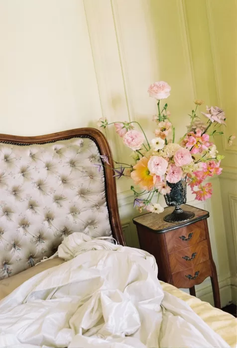 Romantic bedroom scene with an unmade bed and a vase of pastel florals on a wooden nightstand at Château du Prieuré.