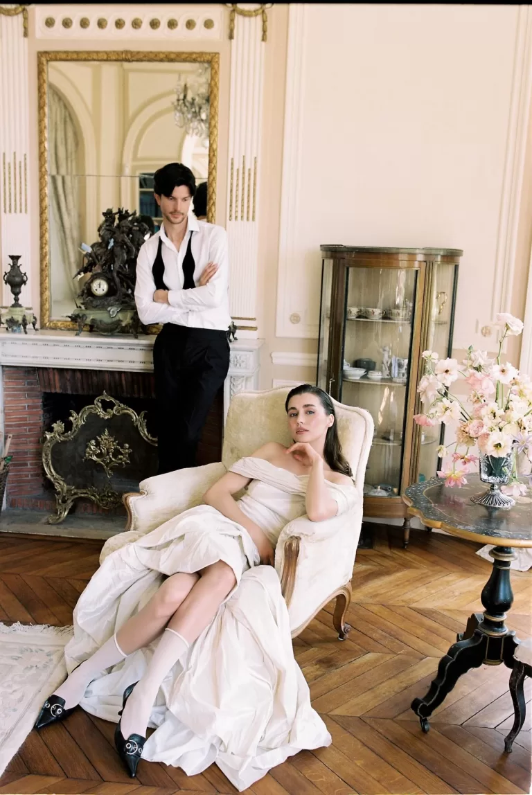 Bride lounging in an antique armchair while the groom stands nearby in a richly decorated room at Château du Prieuré, evoking refined French romance.