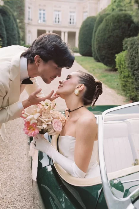 Romantic moment as the groom leans in to kiss the bride seated in a vintage green car at Château du Prieuré.
