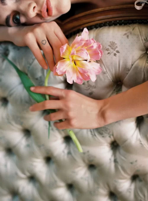 Close-up of the bride’s hand holding a pink tulip while resting on a tufted headboard at Château du Prieuré.