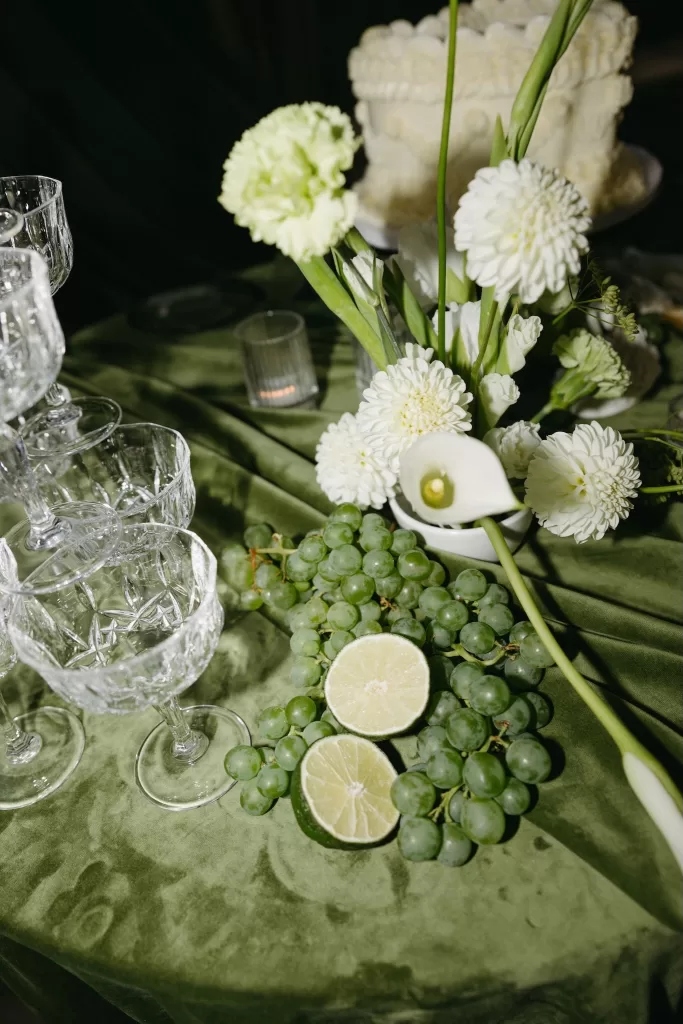 Styled wedding still life with champagne coupes, green grapes, citrus and white florals on velvet linens at Chateau Lill.