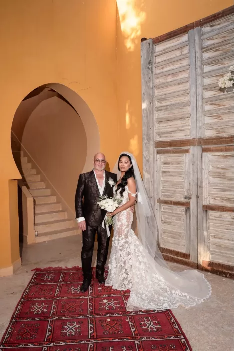 Bride and groom posing beneath an arched doorway and rustic wooden shutters at Jnane Tamsna.