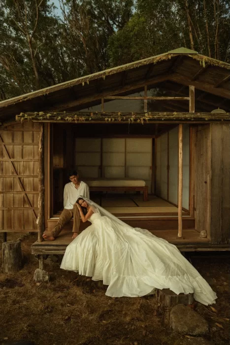 Wide view of the bride reclining against the groom on the porch of Ossipoff’s Cabin, blending rustic architecture and nature.