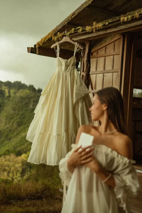 Wedding dress hanging outside Ossipoff’s Cabin while the bride holds a handwritten note, framed by forest scenery.