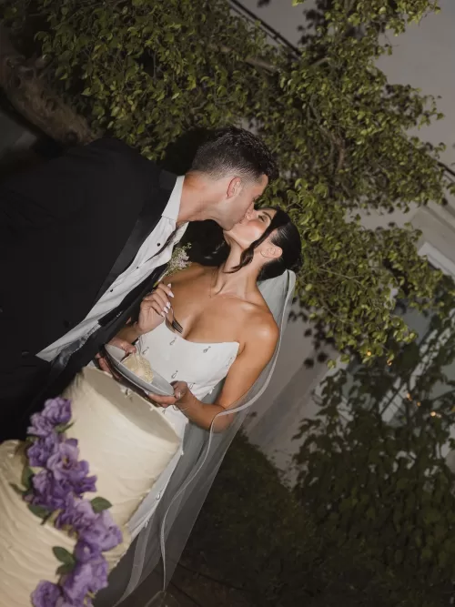 Bride and groom sharing a kiss while cutting their wedding cake at Vandelli Botanical Garden.