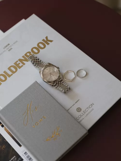 Groom’s watch and wedding rings styled on printed stationery in soft natural light at Vandelli Botanical Garden.