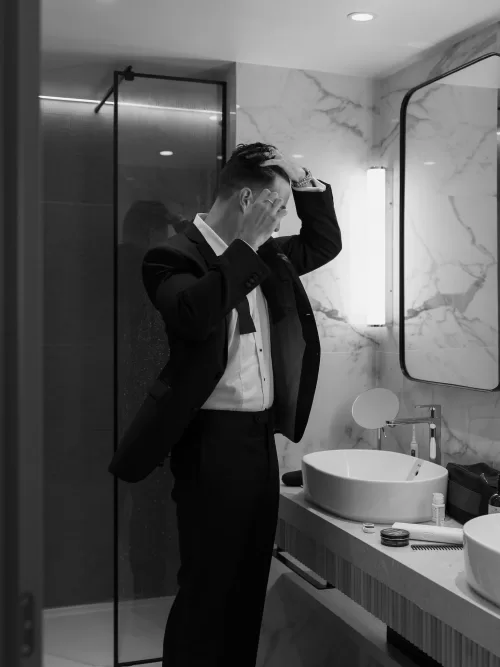 Groom adjusting his hair in a modern bathroom while getting ready at Vandelli Botanical Garden.