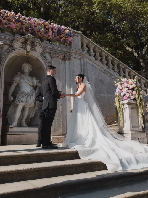 Bride and groom holding hands during their outdoor ceremony on the stone steps at Vandelli Botanical Garden.