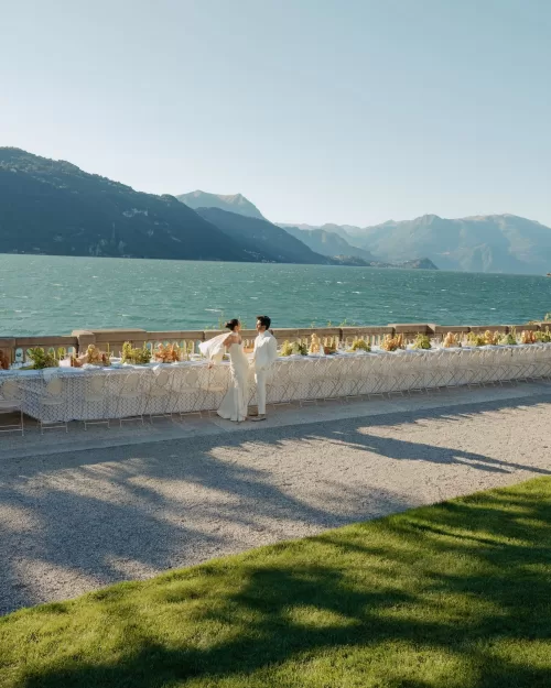 Bride and groom standing beside a long lakeside dinner table at Villa Lario Resort