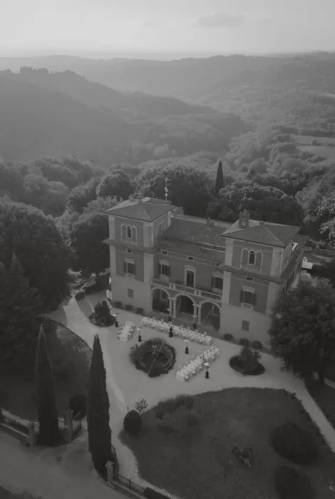 Black and white aerial view of Villa Lena surrounded by rolling Tuscan hills and the reception setup below.