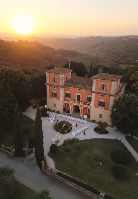 A golden sunset washes over Villa Lena and the surrounding Tuscan hills, with the courtyard set for an outdoor reception.