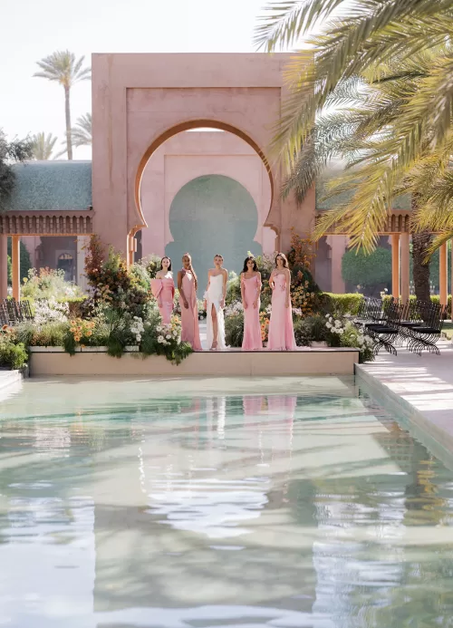 Bridal party standing beside the bride at an Amanjena wedding ceremony framed by arches, palms and floral installations.