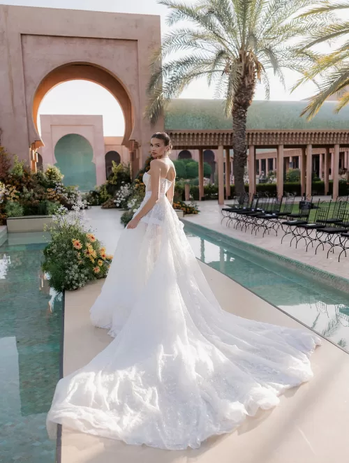 Elegant bridal portrait at Amanjena with the bride standing poolside in a flowing gown framed by arches and palms.