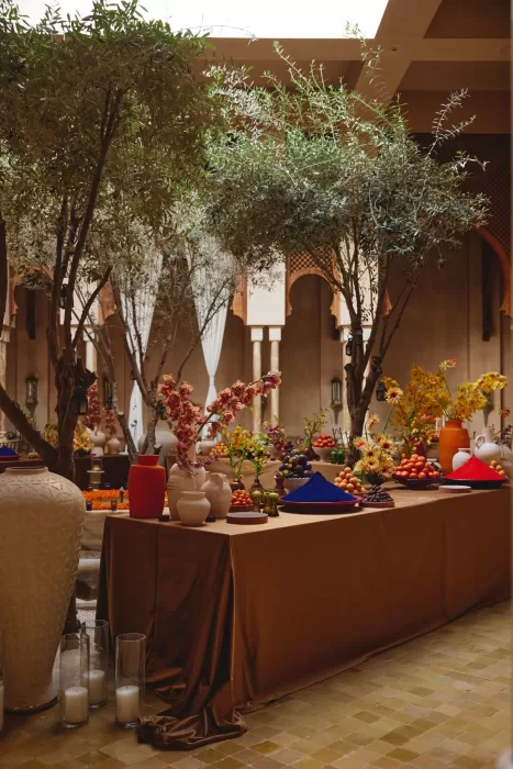 Wedding tables arranged beneath olive trees in the Amanjena courtyard, styled with rich fabrics, florals and vibrant fruit displays.