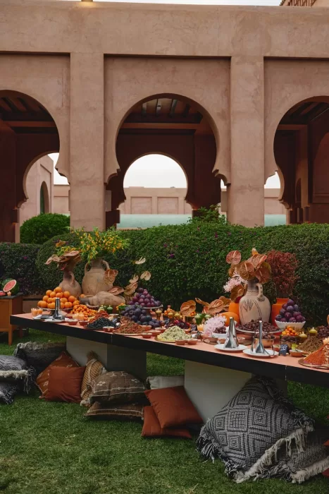 Outdoor wedding feast at Amanjena set beneath arches with Moroccan ceramics, abundant fruit displays and low seating on the lawn.