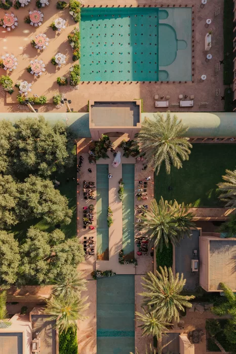 Aerial view of an Amanjena wedding ceremony with guests seated beside long pools, palm trees and courtyard gardens.