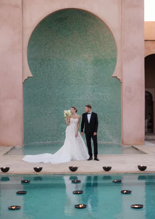 Newlyweds posing together at Amanjena in front of the iconic tiled arch and reflecting pool during golden hour.