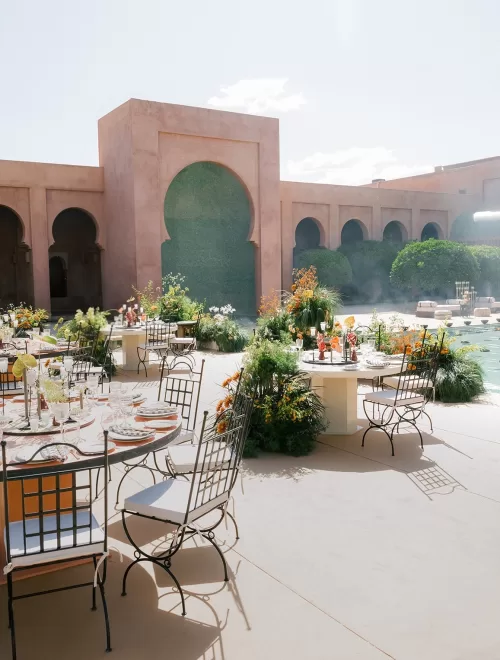 Sunlit courtyard wedding dining at Amanjena with round tables, floral centrepieces and arched Moroccan architecture.