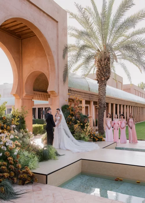 Couple exchanging vows at Amanjena beneath dramatic arches with floral arrangements and reflecting pools.