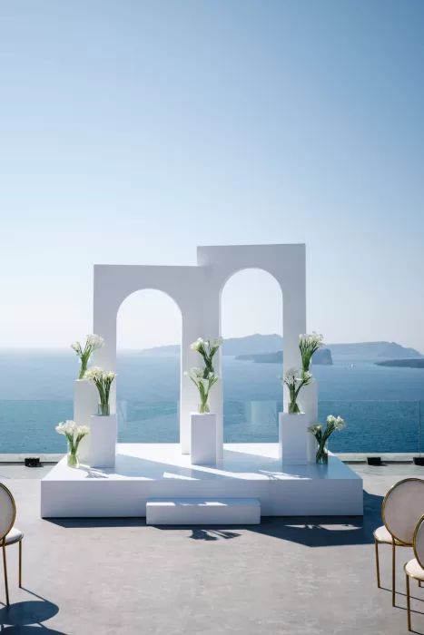 White wedding ceremony arches at Cavo Ventus framed by floral arrangements and uninterrupted views of the Aegean Sea.